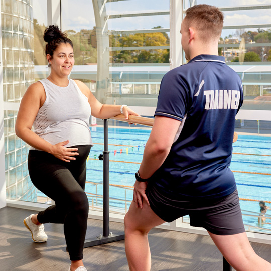 Pregnant woman in a fitness studio with an instructor doing a forward lunge